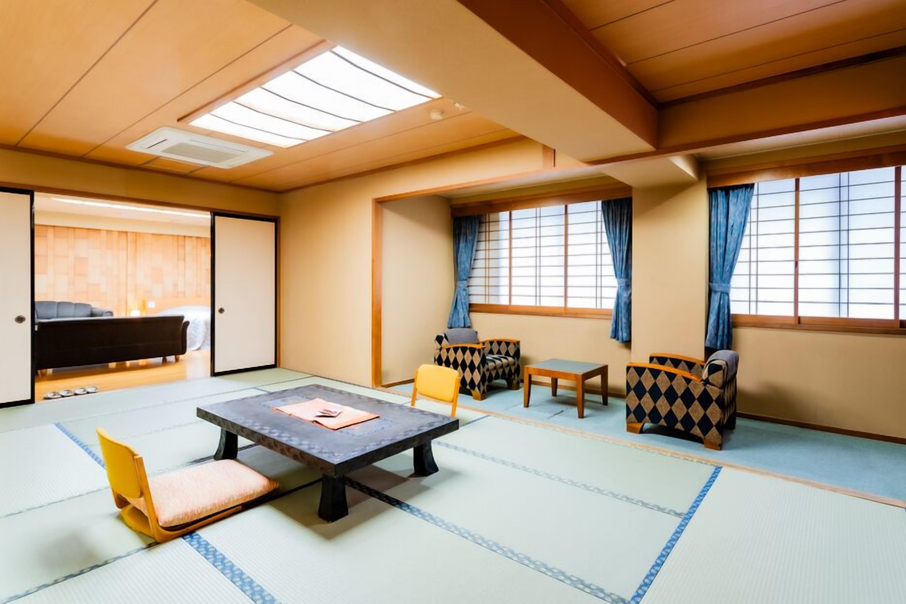Ein Raum mit Tatami-Matten, einem niedrigen Tisch, Stühlen und einer Couch.