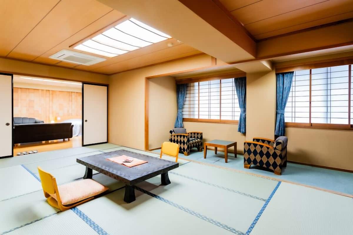 A tatami mat room with a low table, chairs, and a sofa.