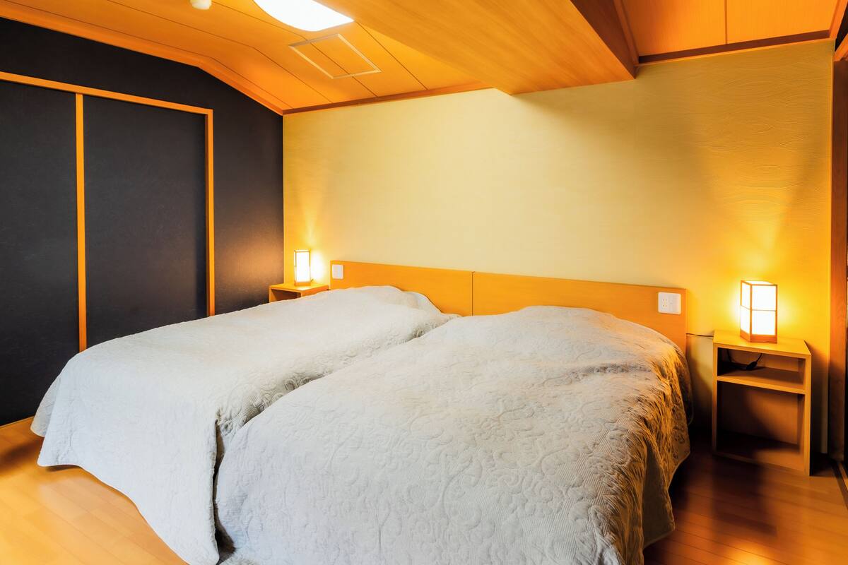 A double bed with a quilt, two bedside tables with lamps, wooden flooring, and a sloped ceiling with recessed lighting.