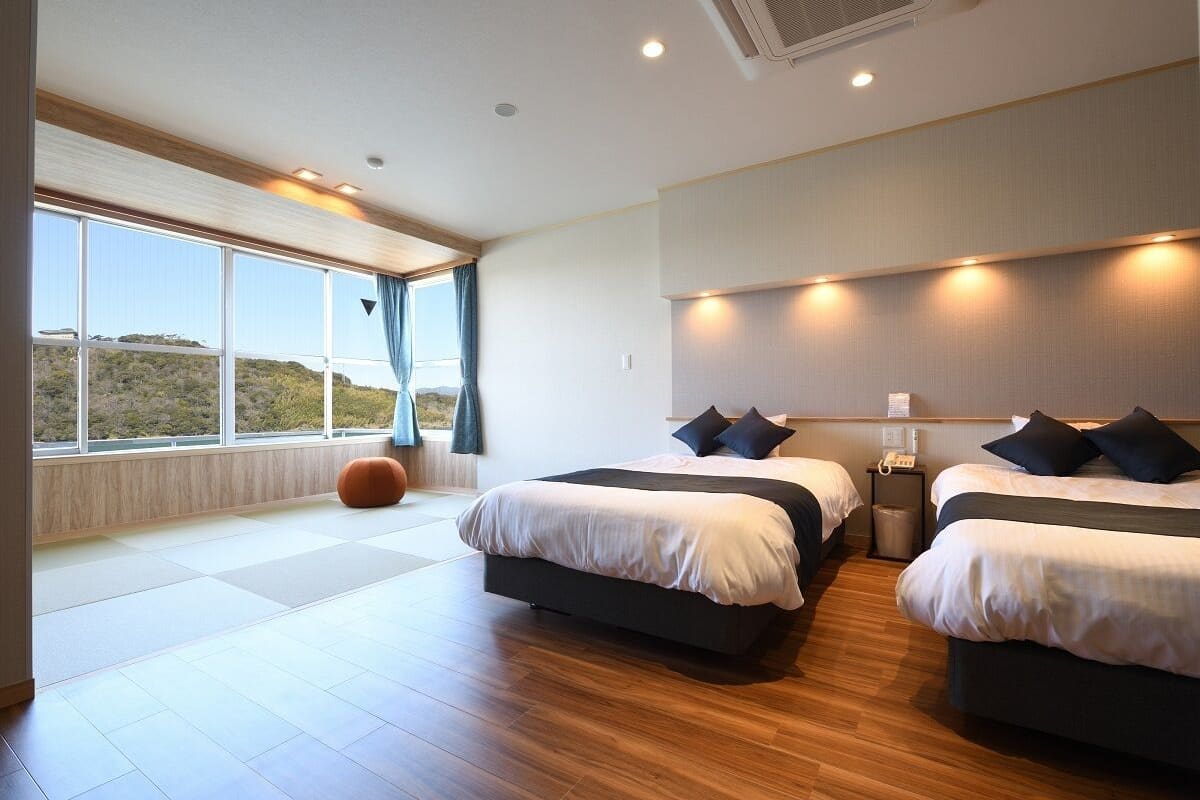 A modern hotel room with two beds, a large window with a view, and a wooden floor.