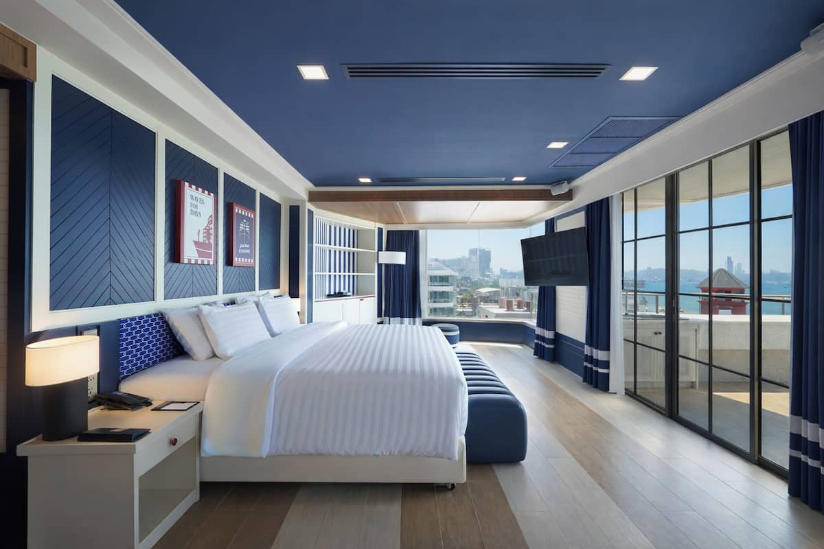 A modern hotel room with a large bed, a desk, a TV, and a city view.