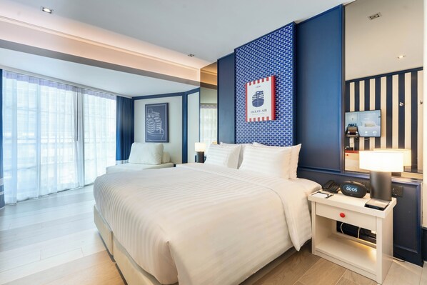 A hotel room with a large bed, bedside table with a lamp, a TV, and a framed picture on the wall.