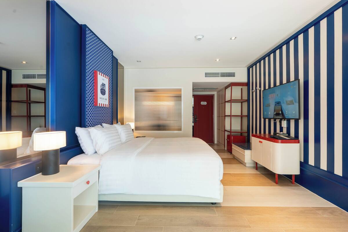 A hotel room with a large bed, bedside tables, a TV, and a wardrobe.