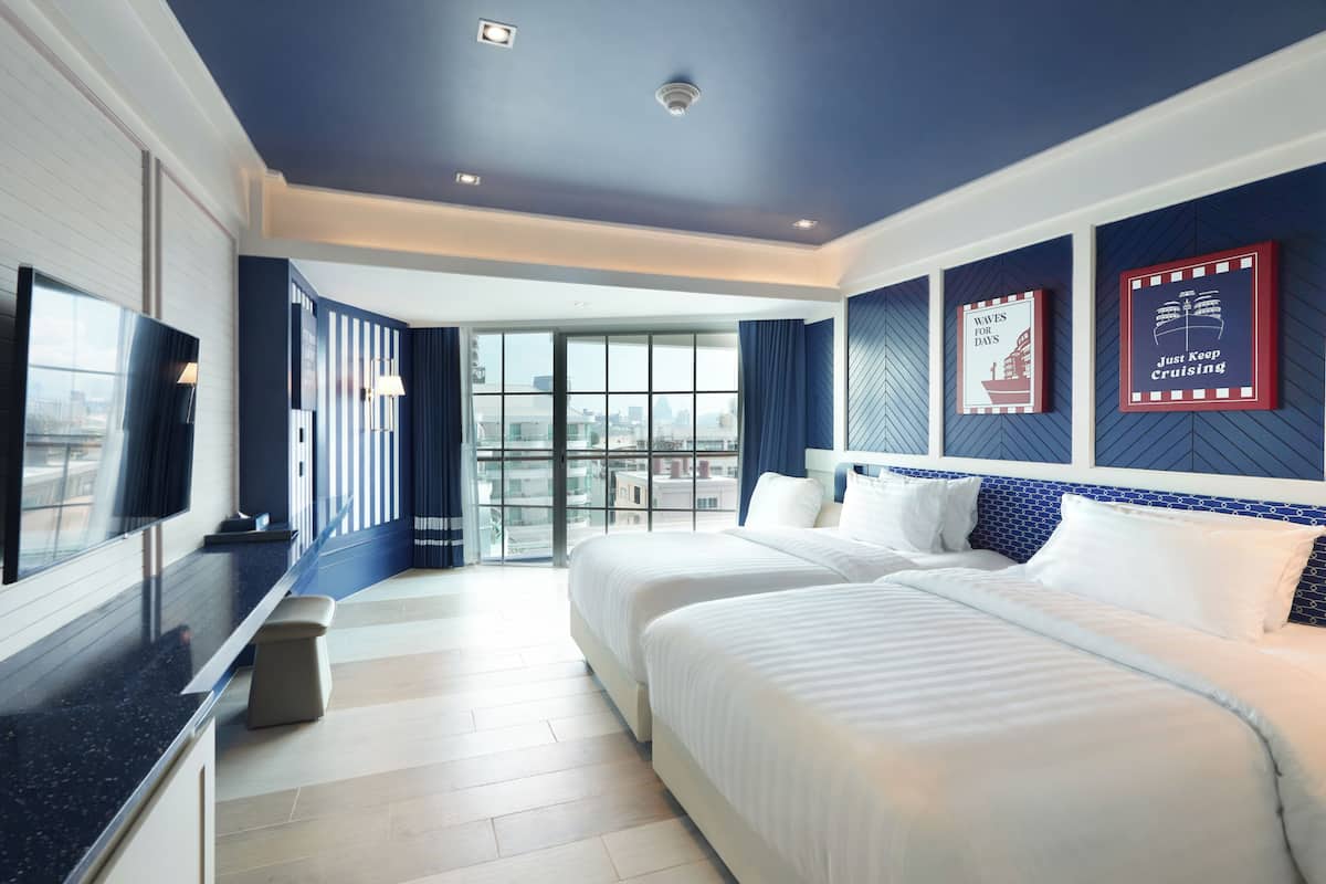 A hotel room with two beds, a TV, a large window, and a city view.