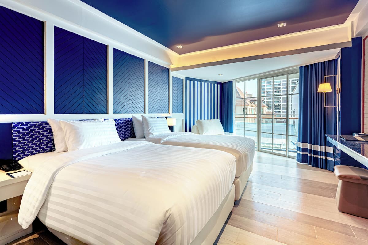 A hotel room with two beds, a desk, a chair, a large window, and a view of the city.