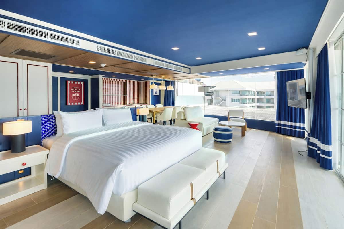 A modern hotel room with a large bed, seating area, and a view of the outside.