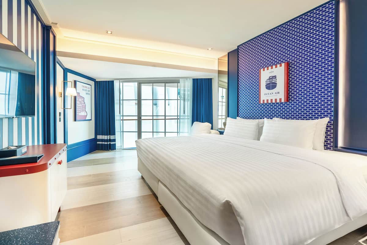 A hotel room with a large bed, a desk, a chair, and a view of the outdoors.