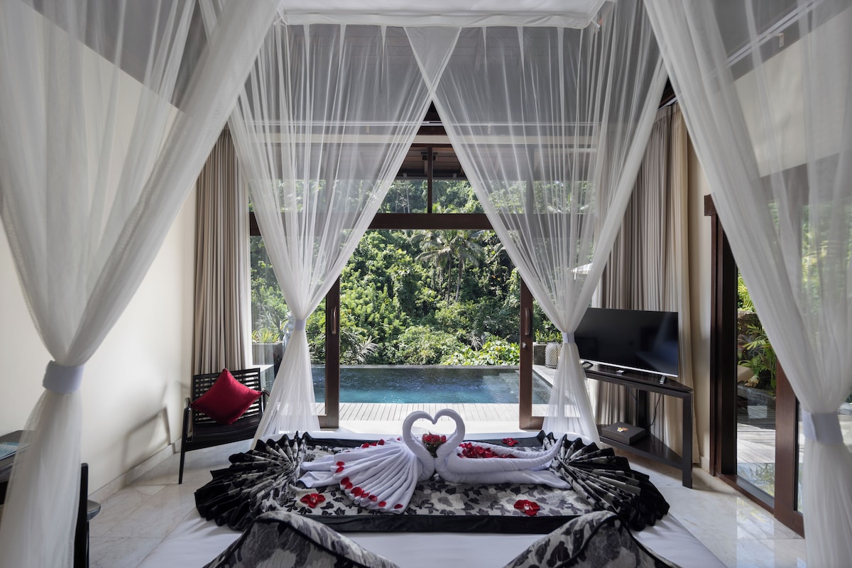 A bedroom with a bed, a TV, and a view of a pool and greenery.