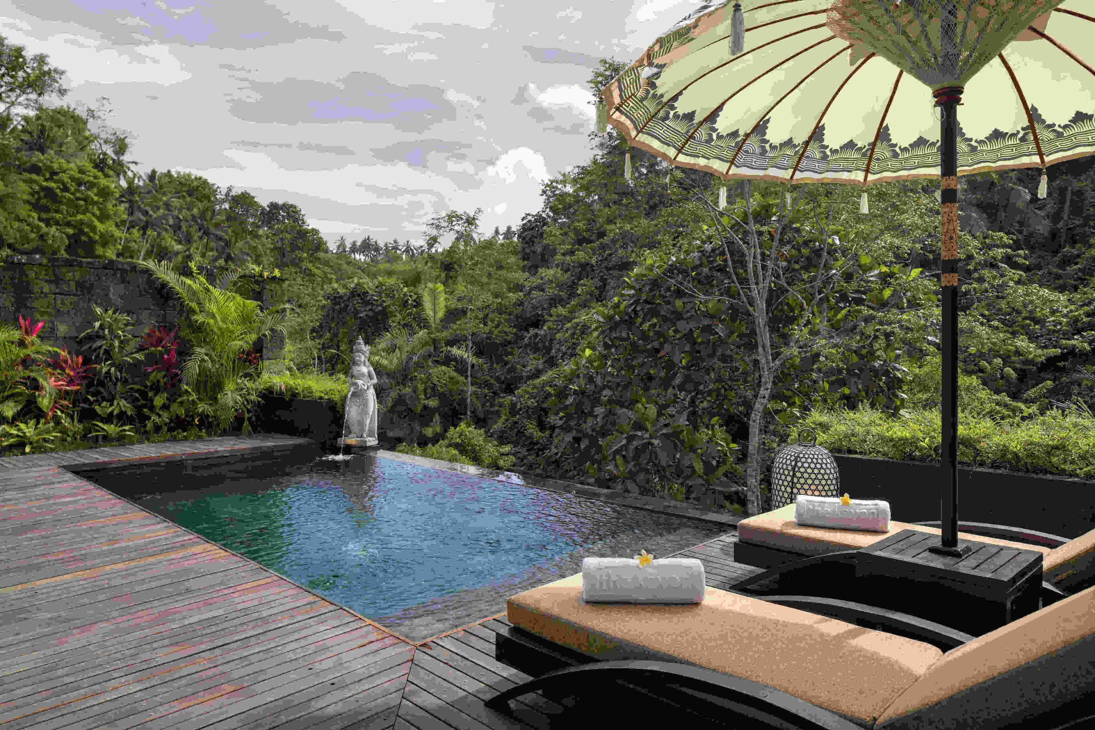 A pool area with lounge chairs, a decorative umbrella, and a statue.
