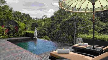 A pool area with lounge chairs, a decorative umbrella, and a statue.