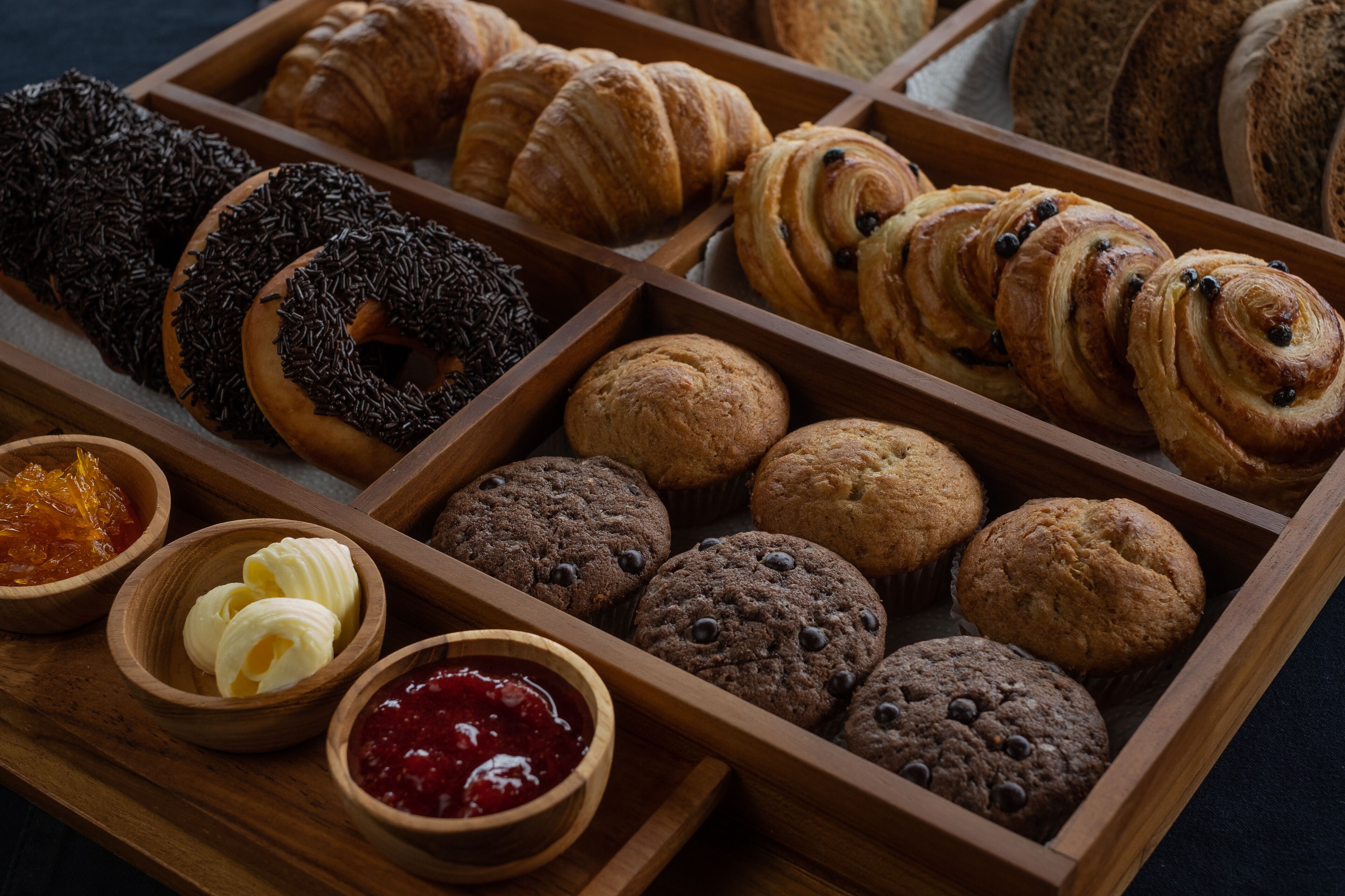 Un plateau en bois contenant divers produits de boulangerie et de petites coupelles de tartinades.