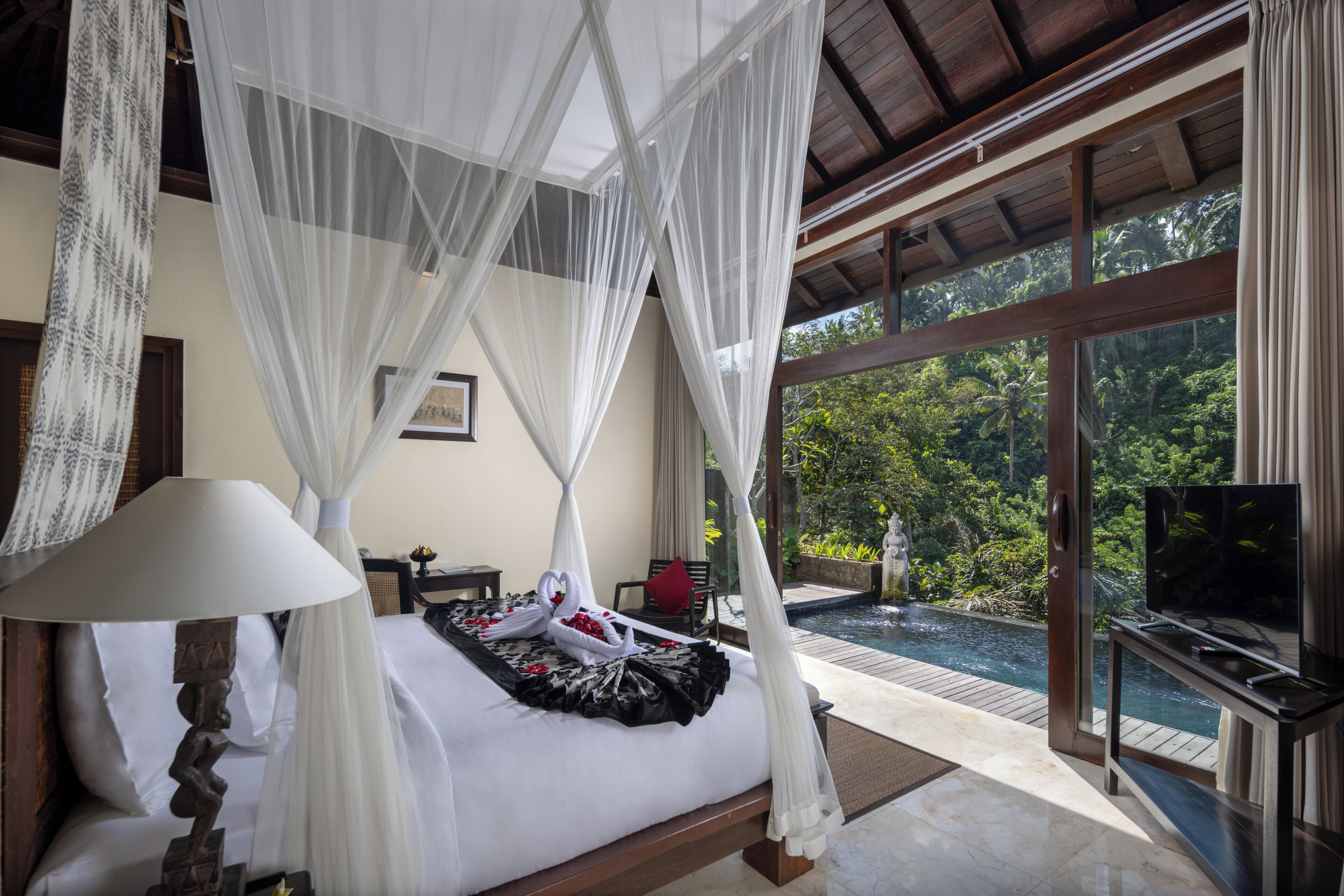 A bedroom with a canopy bed, a television, and a view of a swimming pool and greenery.