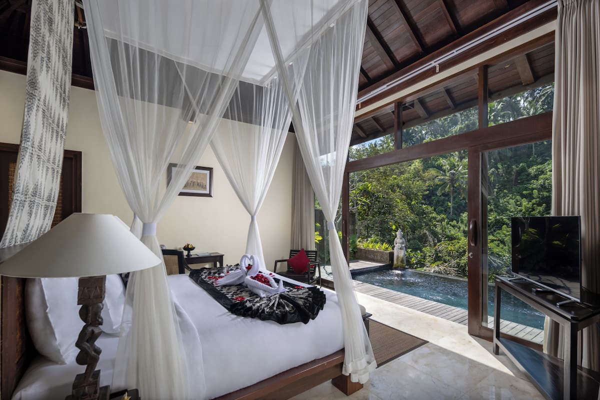 Un dormitorio con cama con dosel, televisor y vistas a una piscina y follaje.