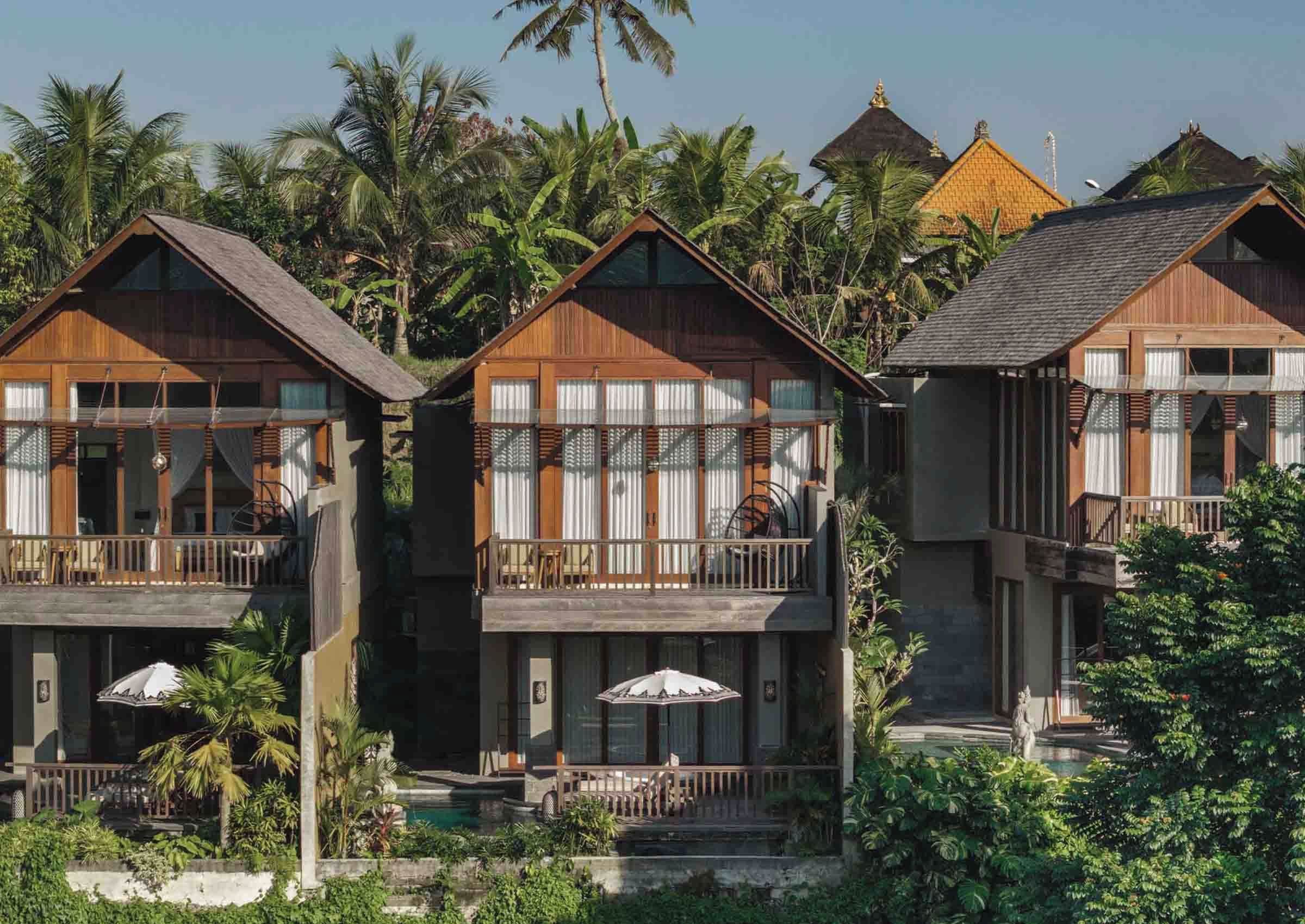 Een rij houten bungalows met balkons, omgeven door weelderige begroeiing en palmbomen.