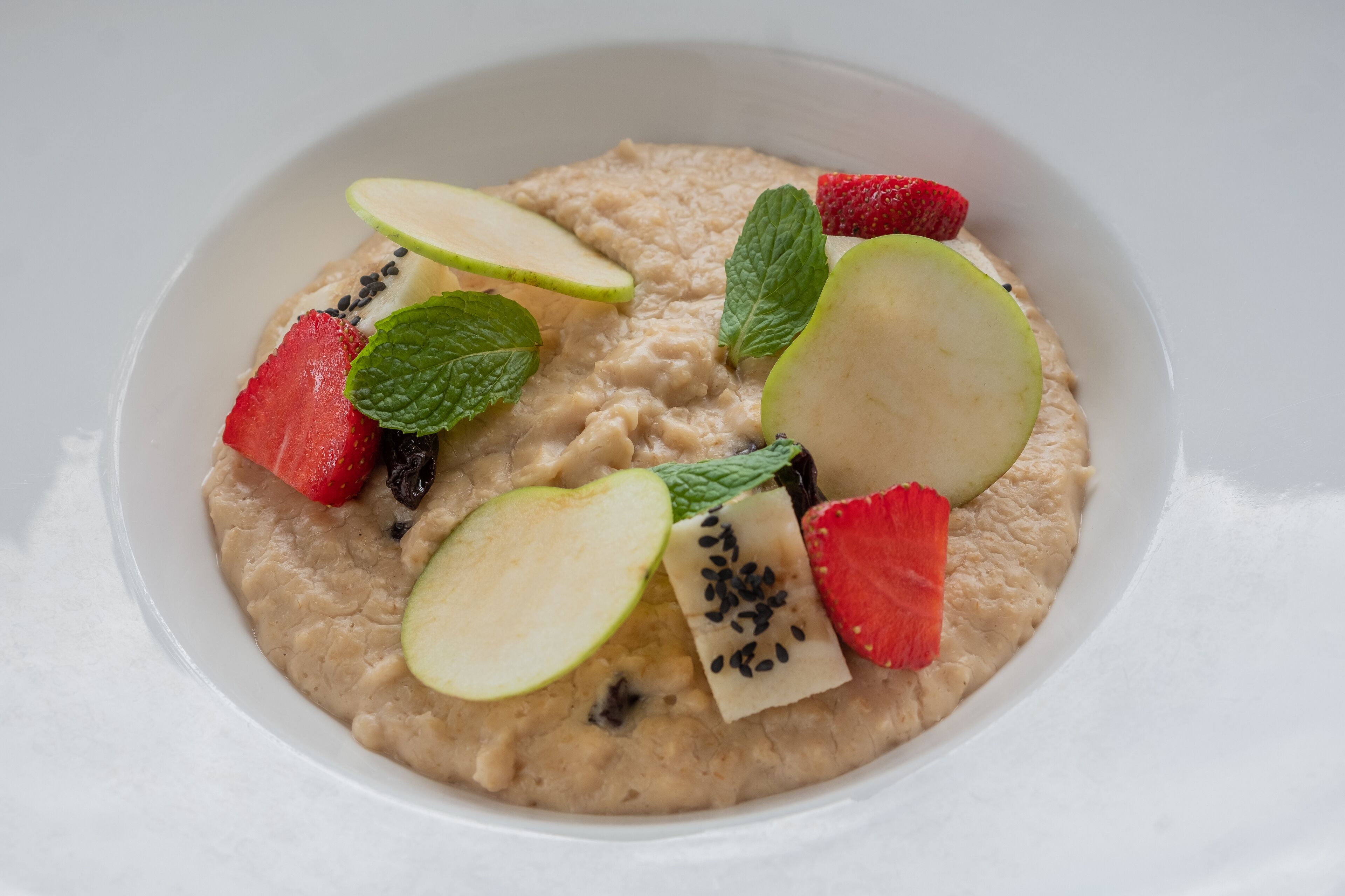 A bowl of oatmeal topped with sliced apples, strawberries, and mint leaves.