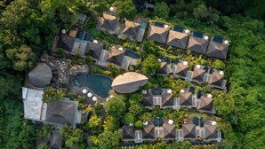 Vista aérea de un complejo turístico con varias cabañas, una piscina central y abundante vegetación circundante.