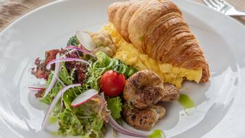 Un plat amb ou serrat, un croissant, bolets a la planxa, i una amanida de verdures mixtes amb rave i un tomàquet de préssec.