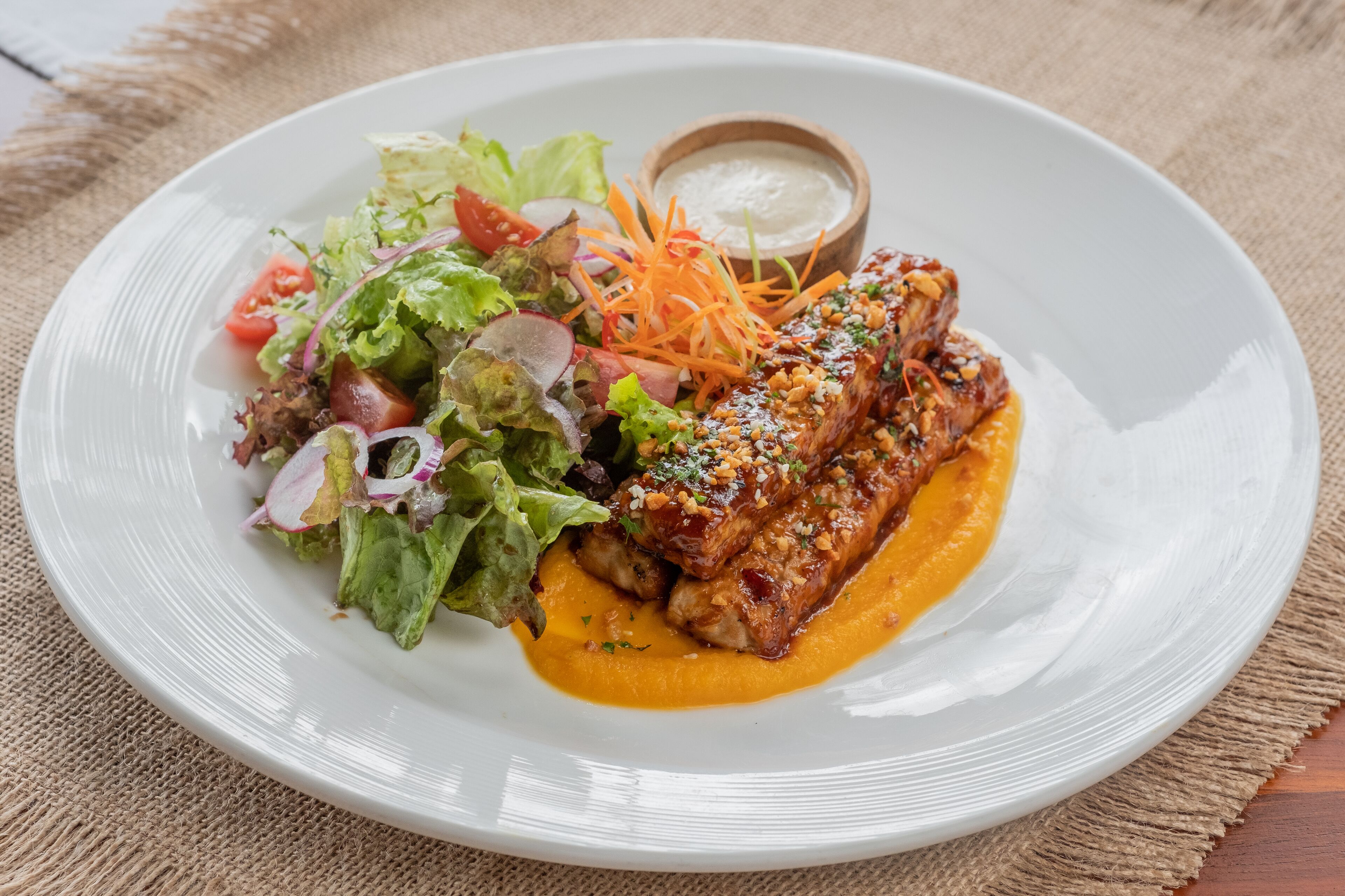 Une assiette de nourriture avec une salade et un petit bol de sauce.