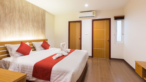 A hotel room with a large bed, wooden headboard, red pillows, a red throw blanket, and a neatly made bed with white towels. - Tee Pak Dee Resident Phuket (Phuket)