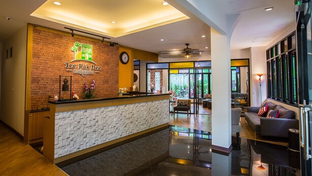 A reception area with a brick wall, a clock, and a counter. - Tee Pak Dee Resident Phuket (Phuket)