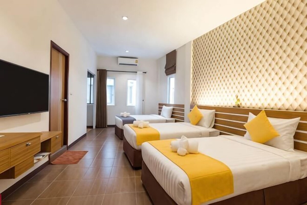 A hotel room with three beds, a TV, a desk, and a patterned headboard.