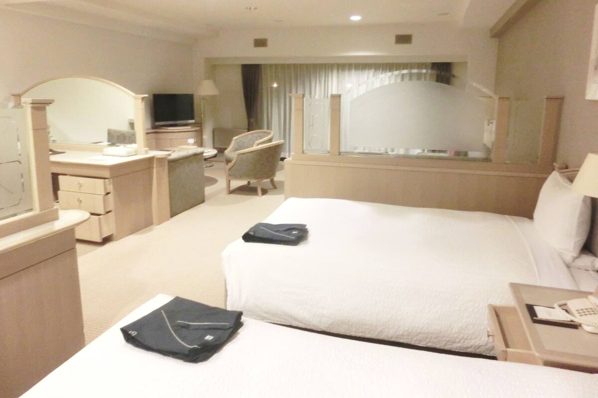Quarto de hotel com uma cama grande, uma mesa, uma cadeira, uma televisão e uma janela com cortinas.