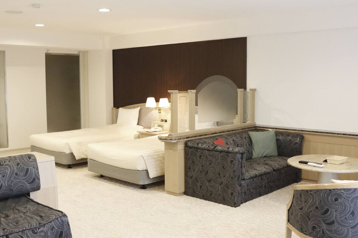 Quarto de hotel com duas camas, um sofá, uma mesinha e um espelho.