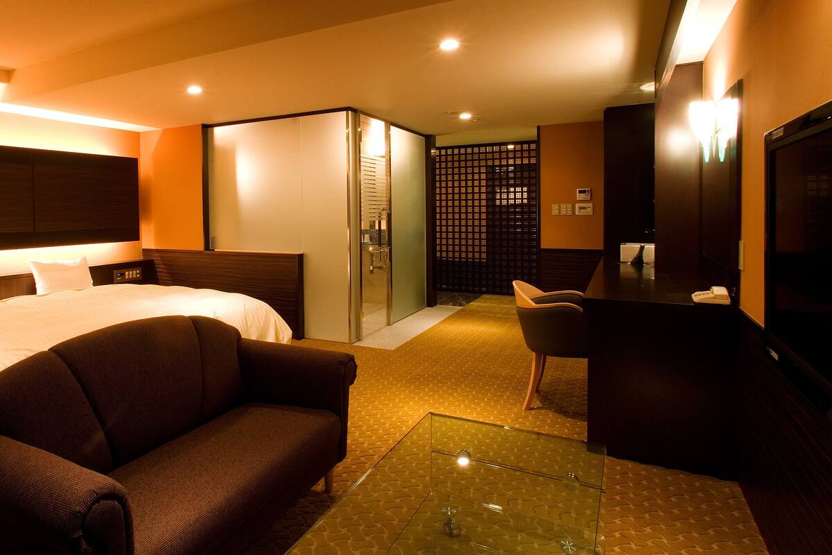 Quarto de hotel com uma cama grande, um sofá, uma escrivaninha e uma televisão.