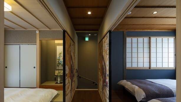 A narrow hallway with a wooden ceiling, a bed on the left, and a window with a view on the right.