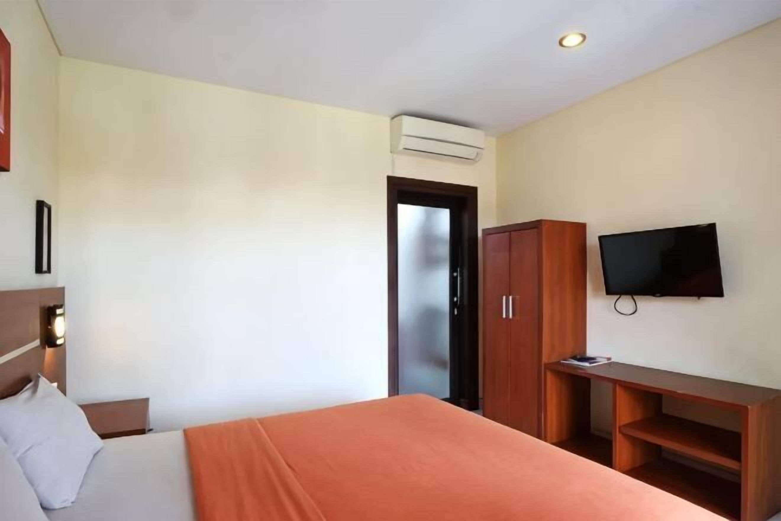 A hotel room with a bed, a TV, a wardrobe, and an air conditioning unit.