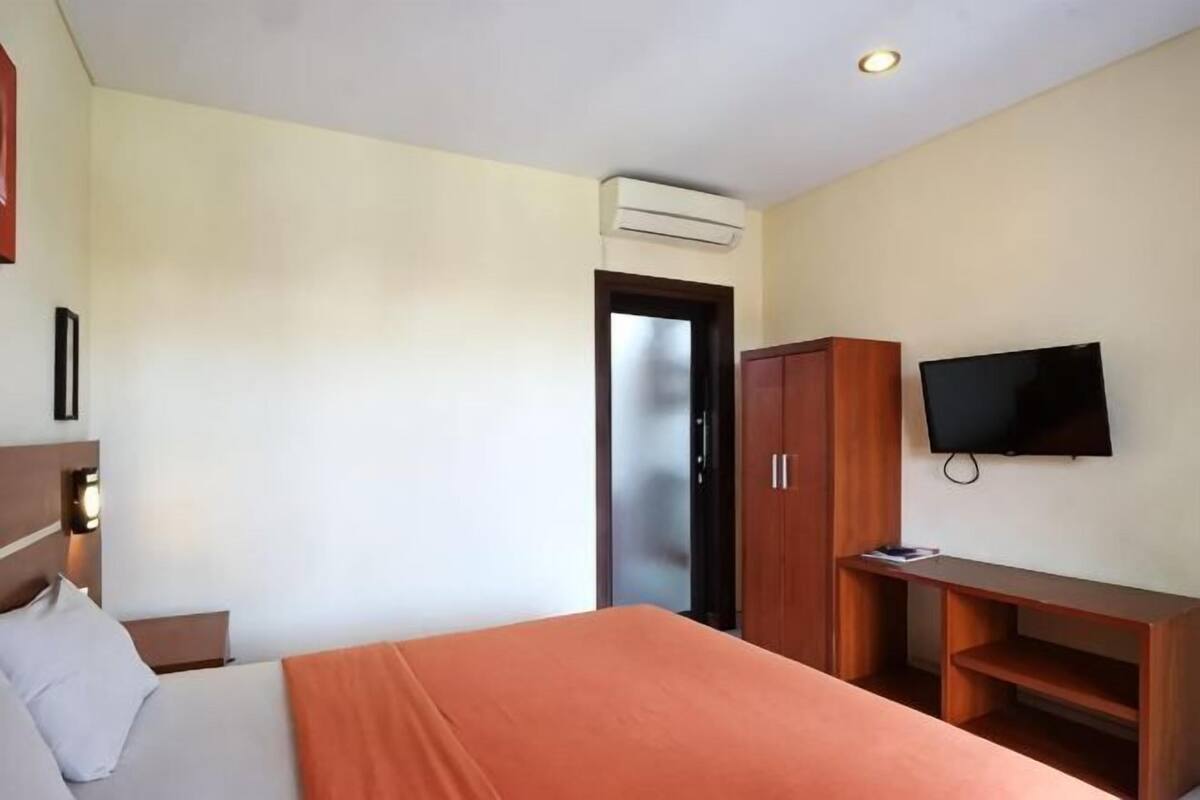 A hotel room with a bed, a TV, a wardrobe, and an air conditioning unit.