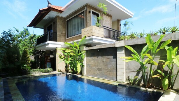 A modern house with a swimming pool, surrounded by lush greenery and a clear blue sky.