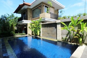 A modern house with a swimming pool, surrounded by lush greenery and a clear blue sky. - Kondra Premiere Guest House Kuta (Kuta)