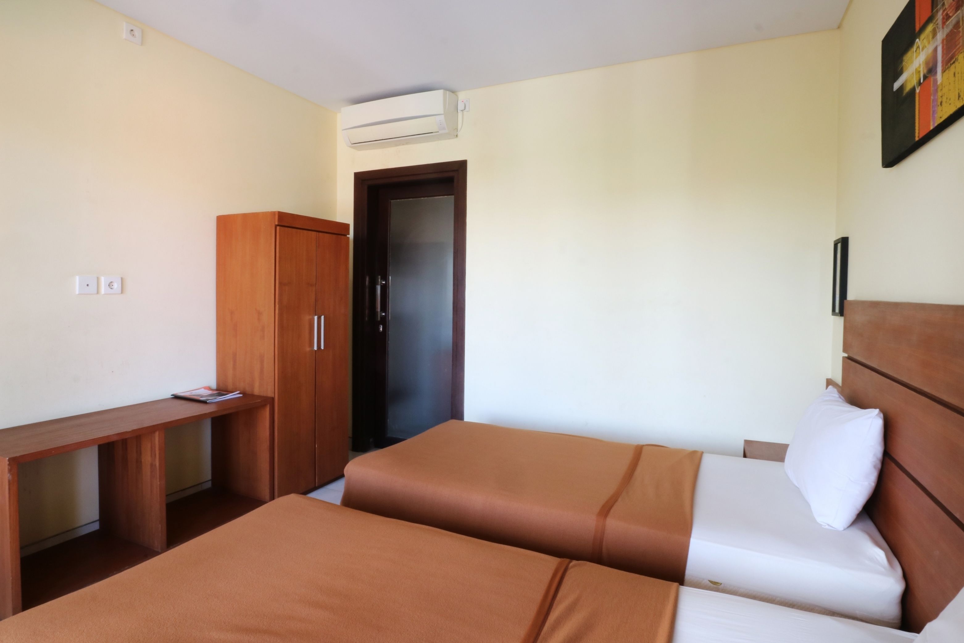 Habitación de hotel con dos camas, un armario de madera, un escritorio y un equipo de aire acondicionado.