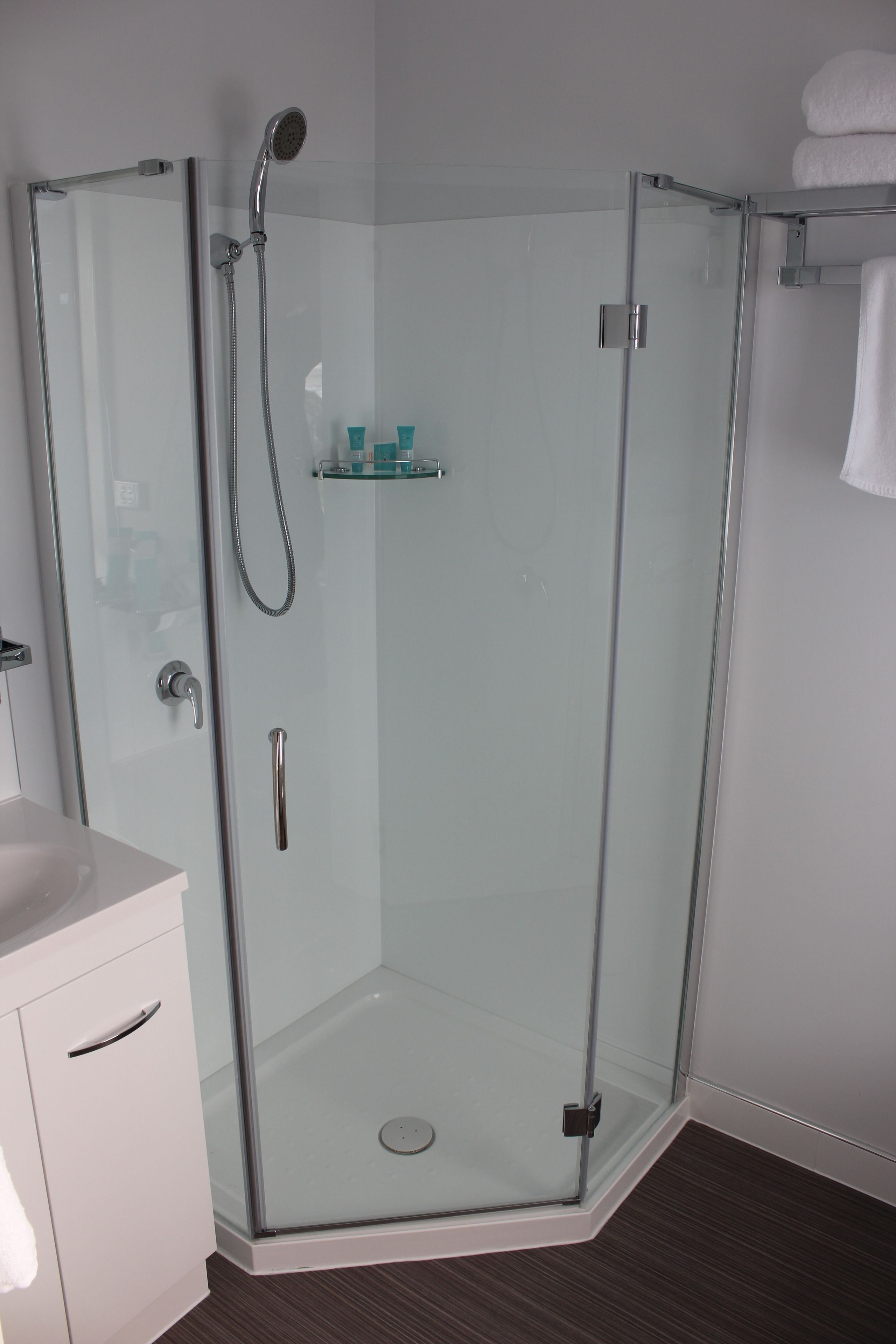 Un baño moderno con ducha de vidrio, lavamanos blanco y un pequeño estante con artículos de aseo.