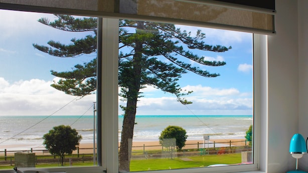 A room with a large window overlooking a beach, a desk, and a lamp. - Beach Hotel (Burnie)