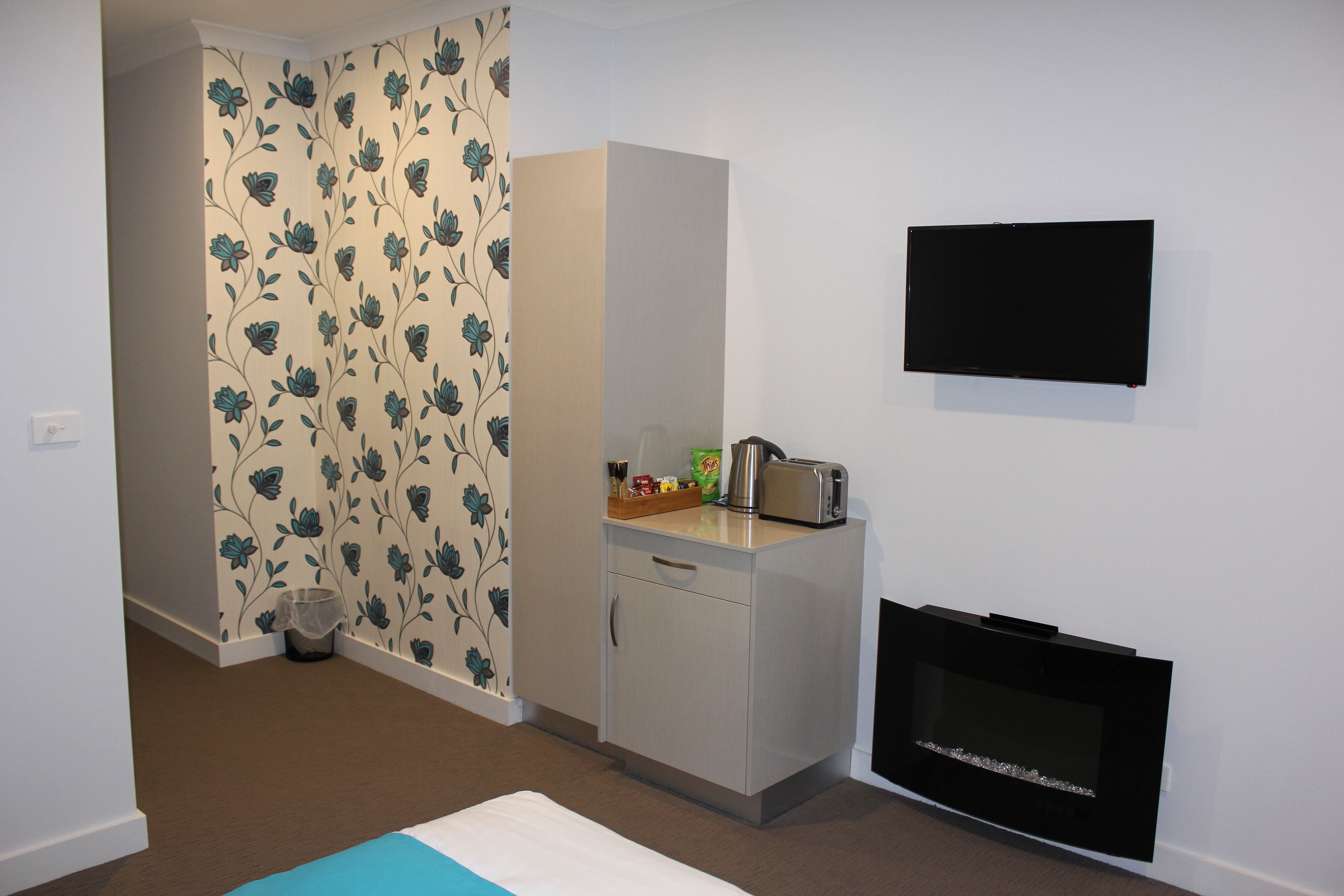 Una habitación con kitchenette, televisor de pantalla plana montado en la pared y papel tapiz estampado.