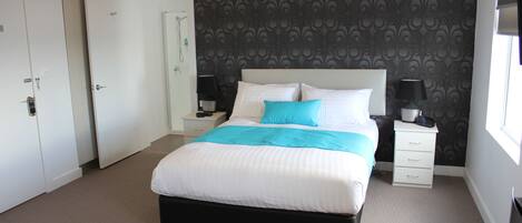 A neatly arranged hotel room with a large bed, a bedside table with a lamp, a wardrobe, and a bathroom door.