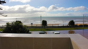 A coastal view with a beach, a road with cars, and a clear sky. - Beach Hotel (Burnie)