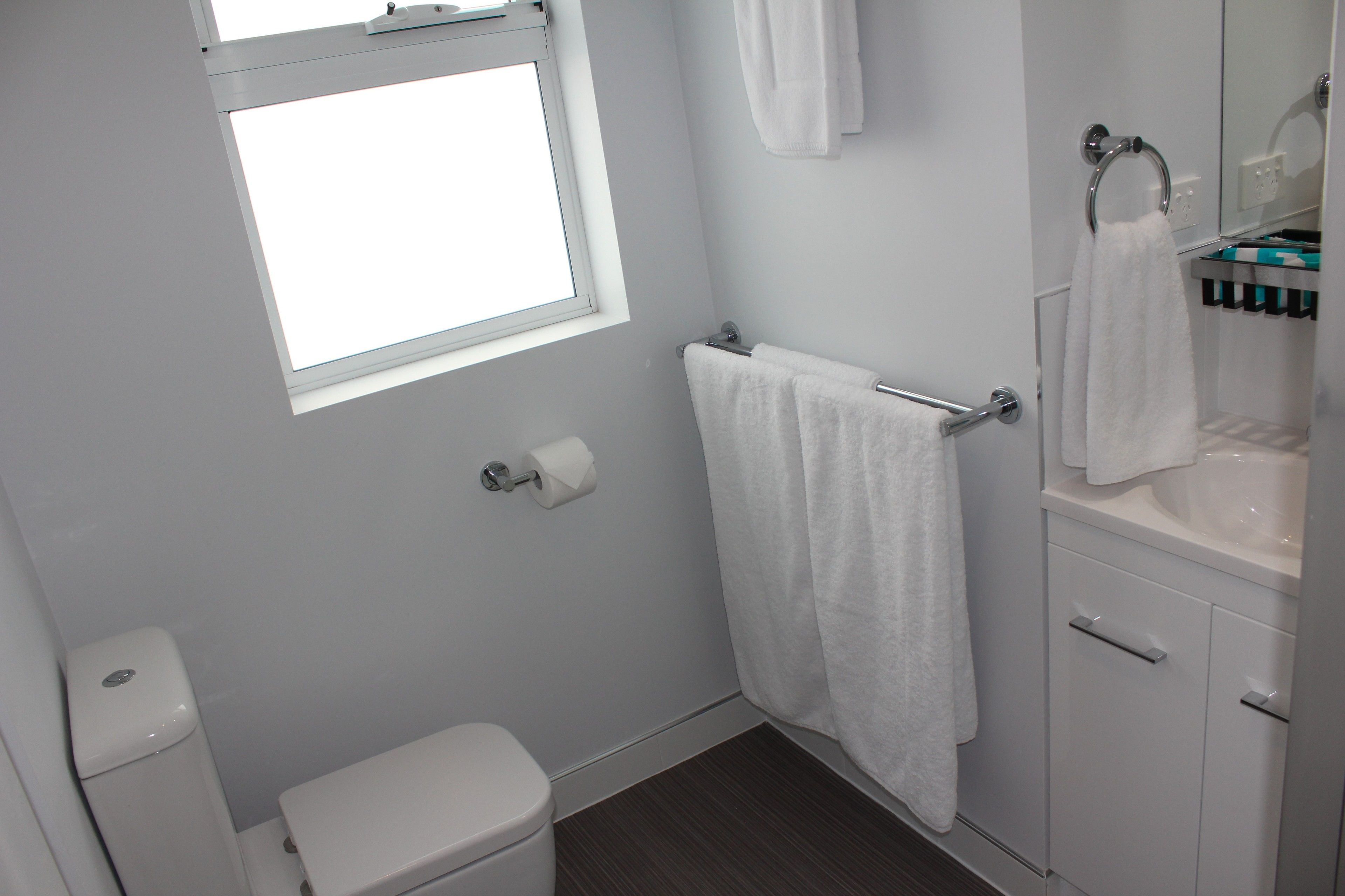 A bathroom with a toilet, a towel rack, a sink, and a window.