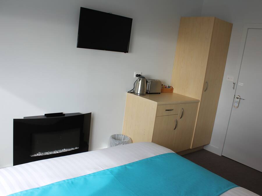 A hotel room with a bed, a TV, a kitchenette, and a wardrobe.