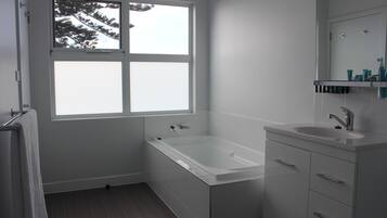Un baño moderno con bañera, lavamanos y ventana con vistas a árboles.