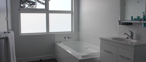 A modern bathroom with a bathtub, a sink, and a window with a view of trees.