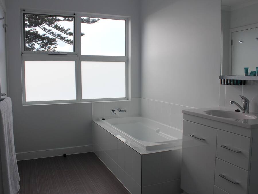 Un baño moderno con bañera, lavamanos y ventana con vistas a árboles.