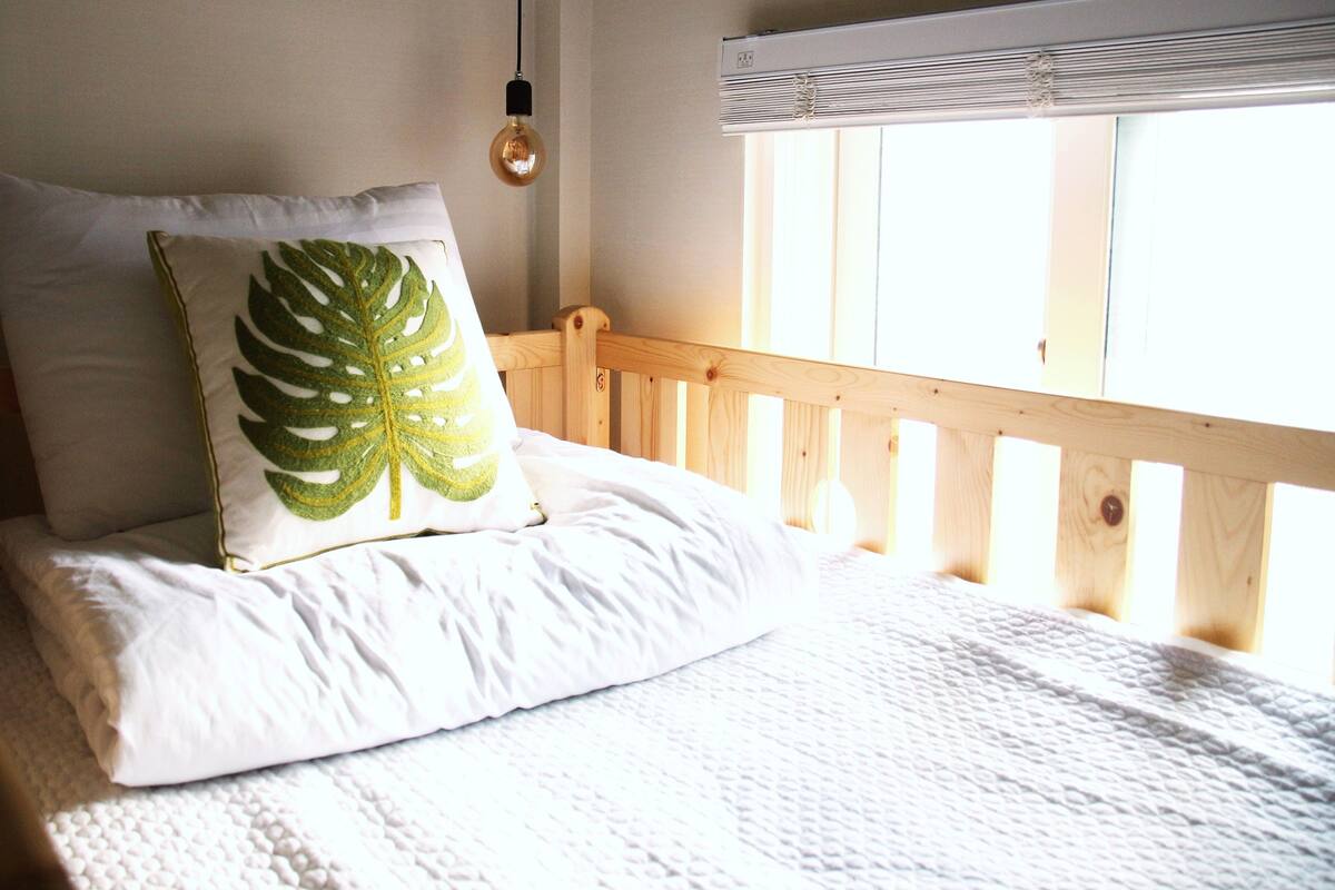 Un lit avec une literie blanche, un oreiller orné d’une feuille verte et une tête de lit en bois.