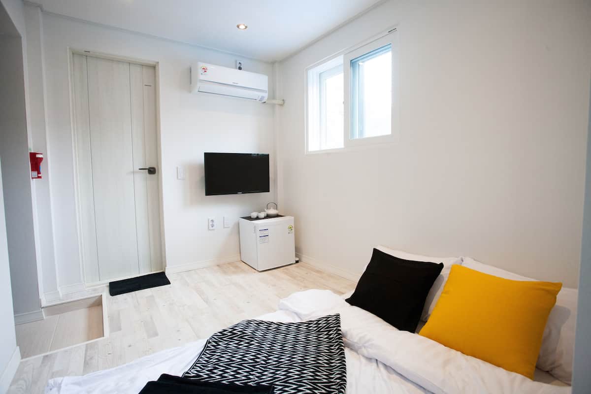 Une chambre à coucher avec un lit, une télévision, une petite armoire blanche et une fenêtre.