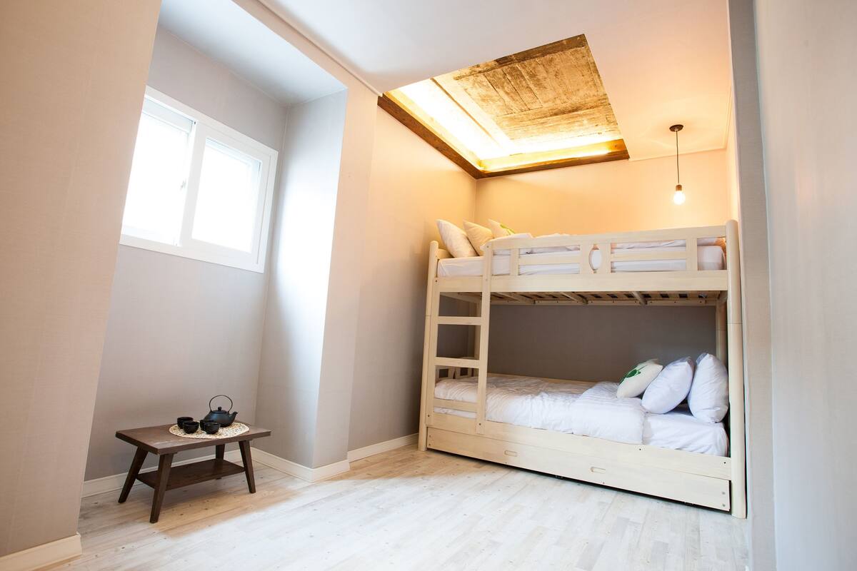 Une chambre avec un lit superposé, une petite table avec une théière et des tasses, et une lucarne au-dessus du lit.