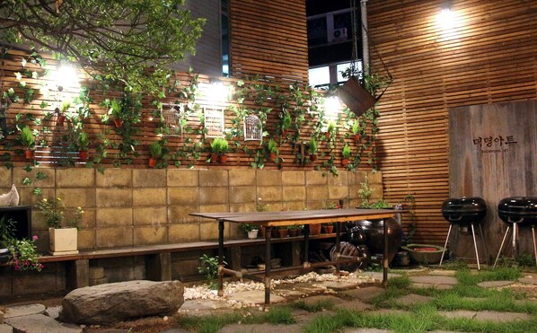 An outdoor seating area with a wooden table and benches, surrounded by potted plants and a stone wall.