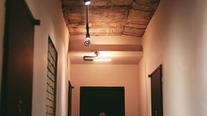 Un pasillo estrecho con un aplique de techo, una puerta con placa de número y una lámpara en la pared.
