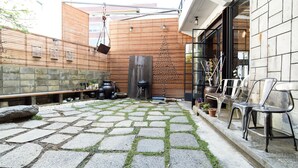 Un patio con baldosas de piedra, cerca de madera, una parrilla y mobiliario para exteriores.